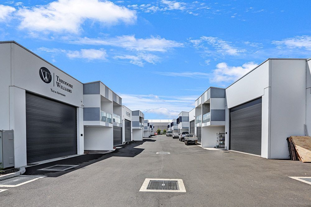A row of modern industrial buildings with gray roller doors, blue sky overhead.