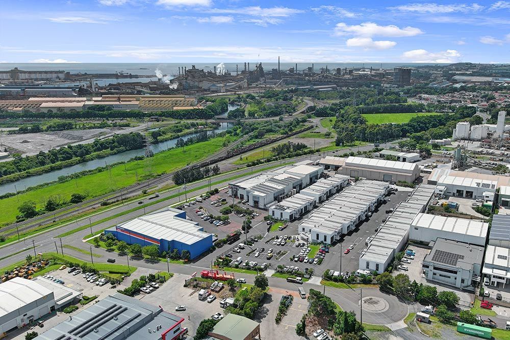 Aerial view: Industrial area with buildings, river, highway, and city in the background.