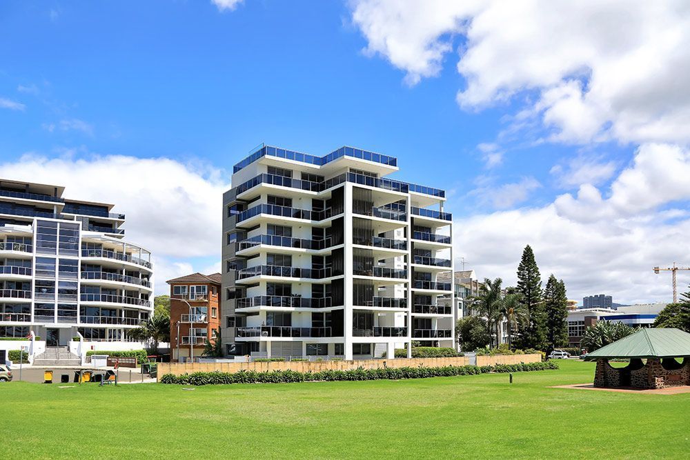 Modern white apartment building with blue accents, blue sky, and green grass.