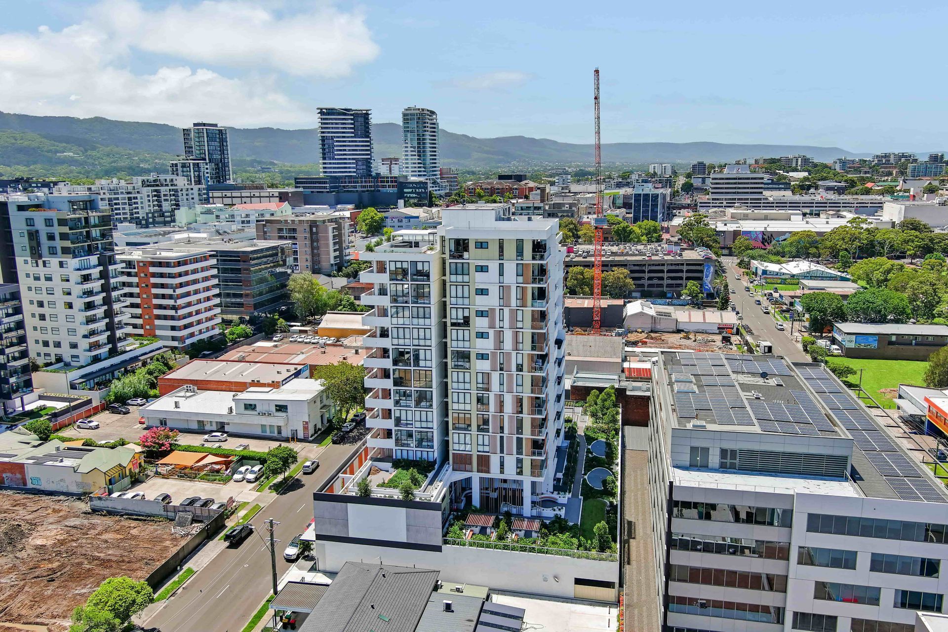 Cityscape with multi-story buildings, including an apartment tower and industrial area, under a blue sky.