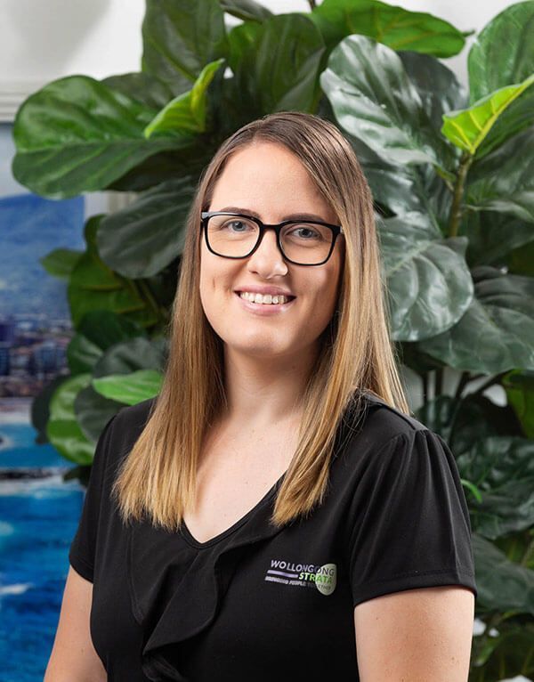 Woman with glasses smiles in a black top, with a large plant in the background.