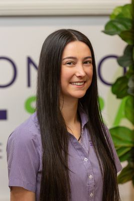 Young woman with long black hair smiling, wearing a purple striped shirt, standing indoors.