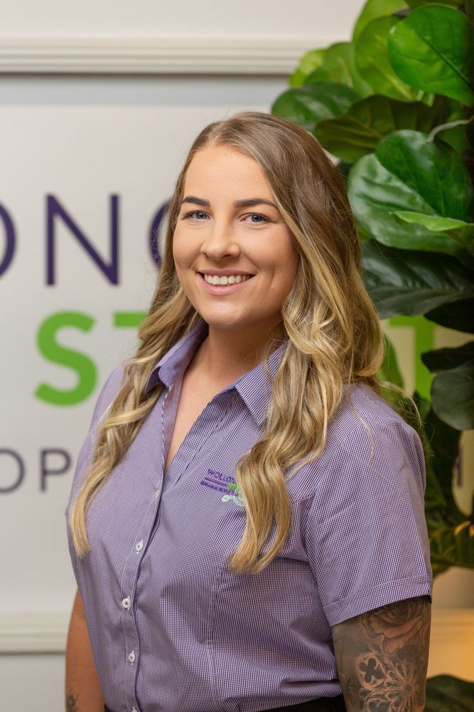 Woman with blonde hair and a purple striped shirt smiles, posing indoors.