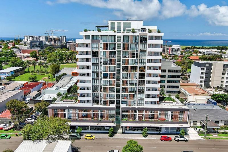 Modern high-rise apartment building with retail space on a sunny day, near a park and the ocean.