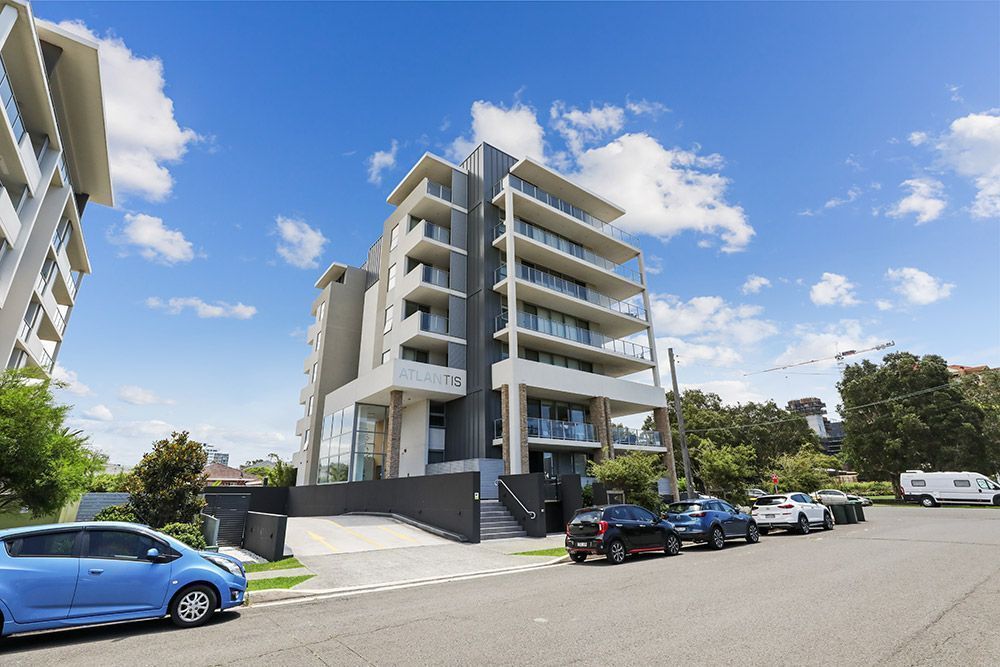Modern multi-story apartment building with balconies. Cars parked on street in front.