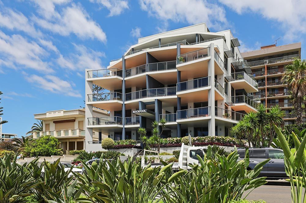 Modern apartment building with balconies, blue sky, and foliage.
