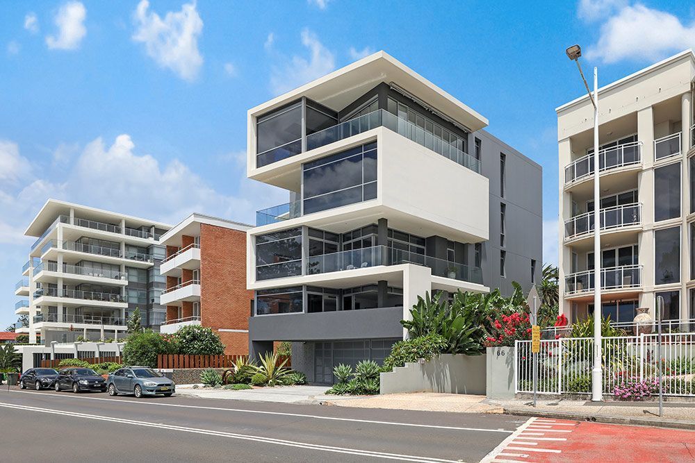 Modern apartment buildings on a city street; grey, white and brown exteriors, blue sky.