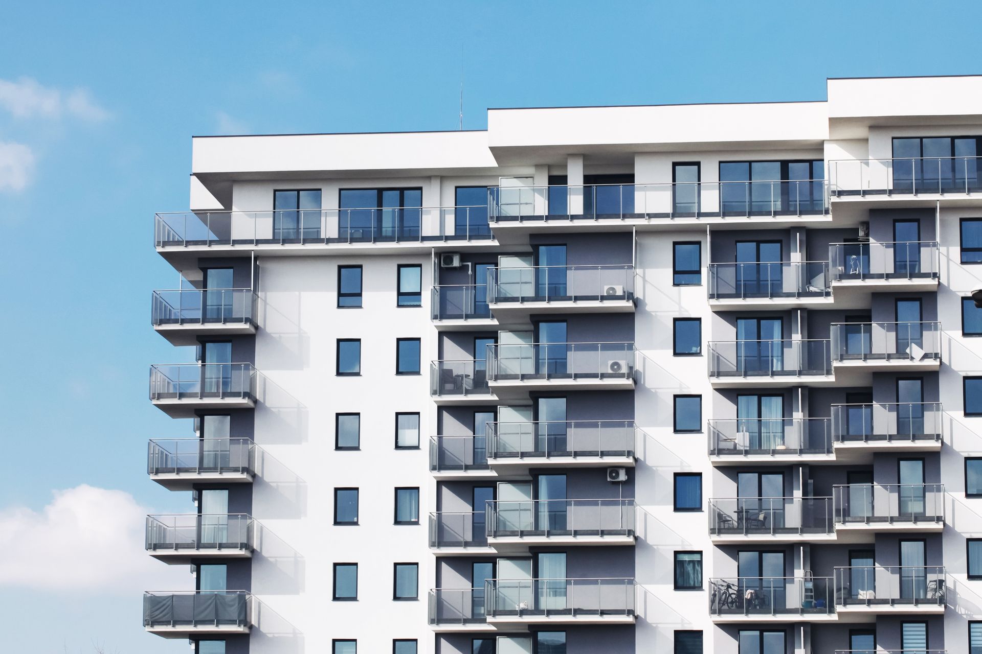 White apartment building with multiple balconies against a blue sky.