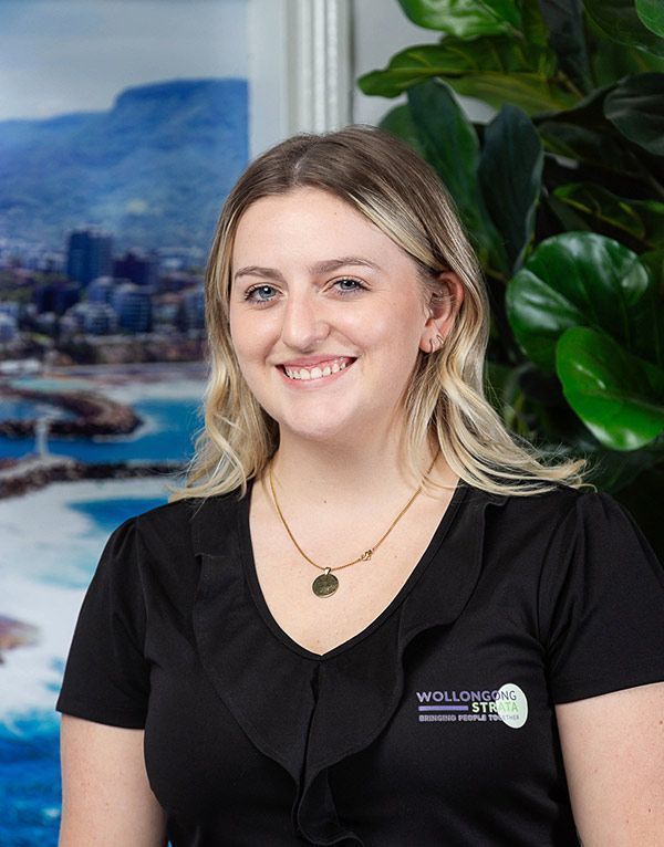 Blonde woman with a friendly smile wearing a black shirt, against a coastal backdrop.