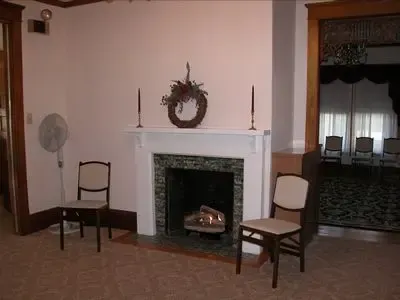 Fireplace with candles and a wreath, flanked by chairs, and an open doorway to another room.