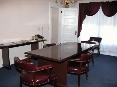 Meeting room with a large brown table, red chairs, white door, and maroon curtains.