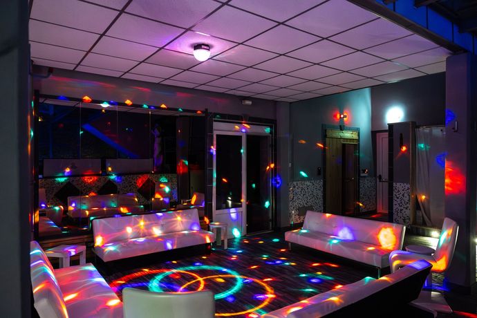 Luci da discoteca colorate sopra un moderno salotto con divani, un tavolo e grandi finestre di notte