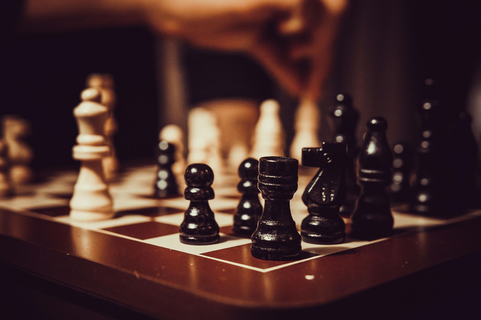 A person is playing a game of chess on a wooden chess board.