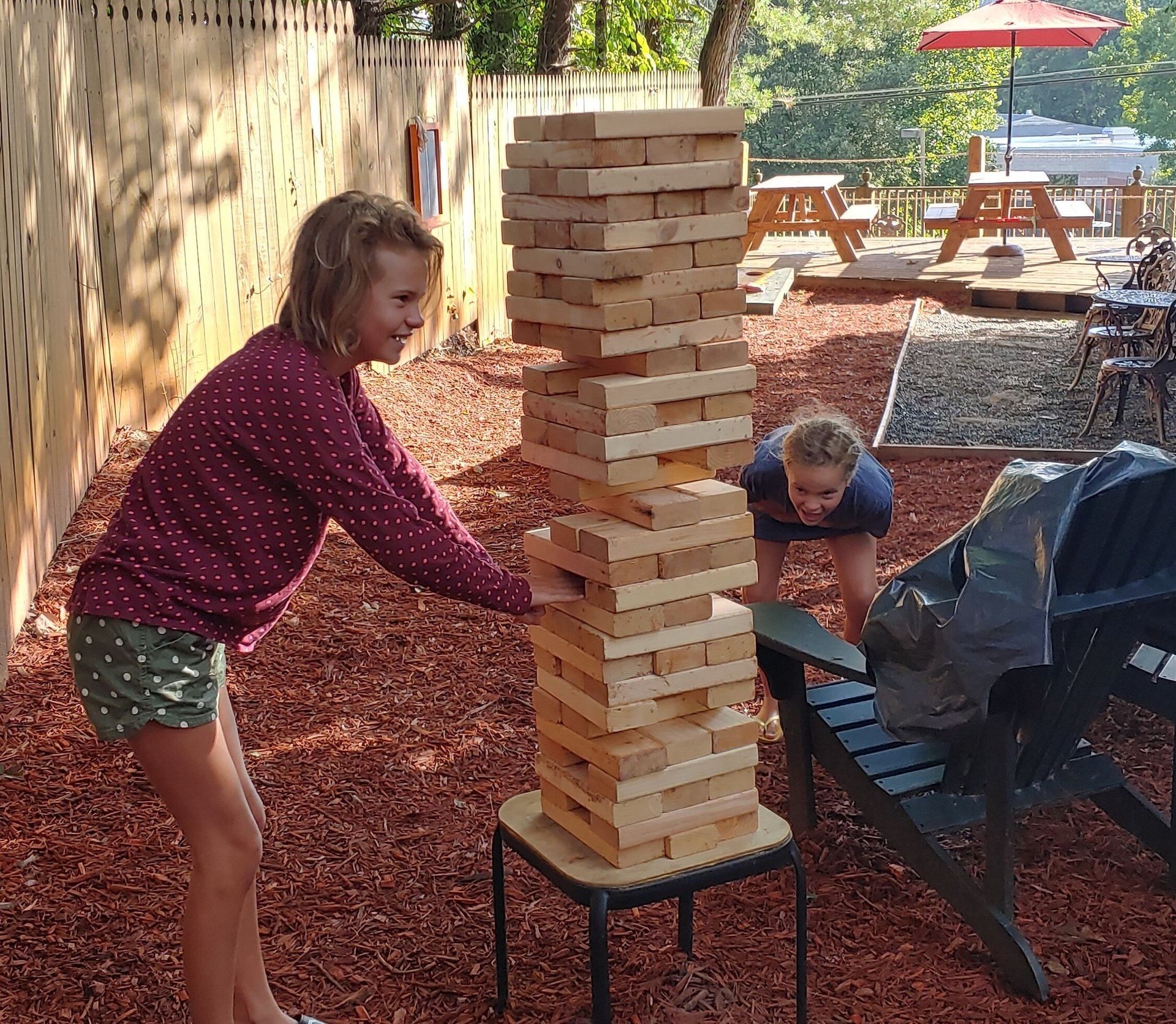 People playing giant Jenga outdoors on a patio, one stack nearly collapsing