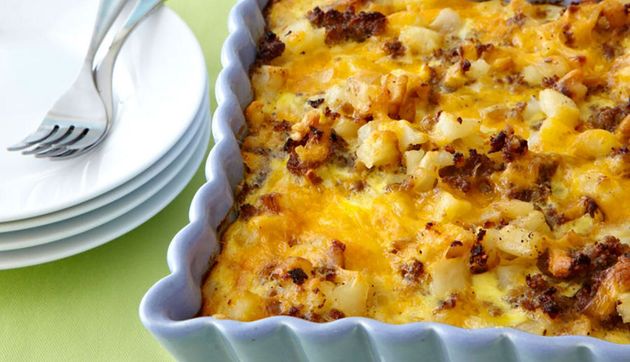 Baked casserole in a blue dish beside stacked white plates and forks on a green tablecloth