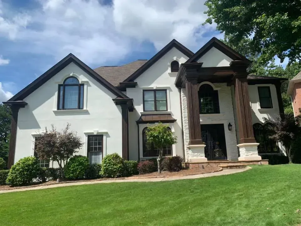 A large white house with brown trim sits on a lush green hillside