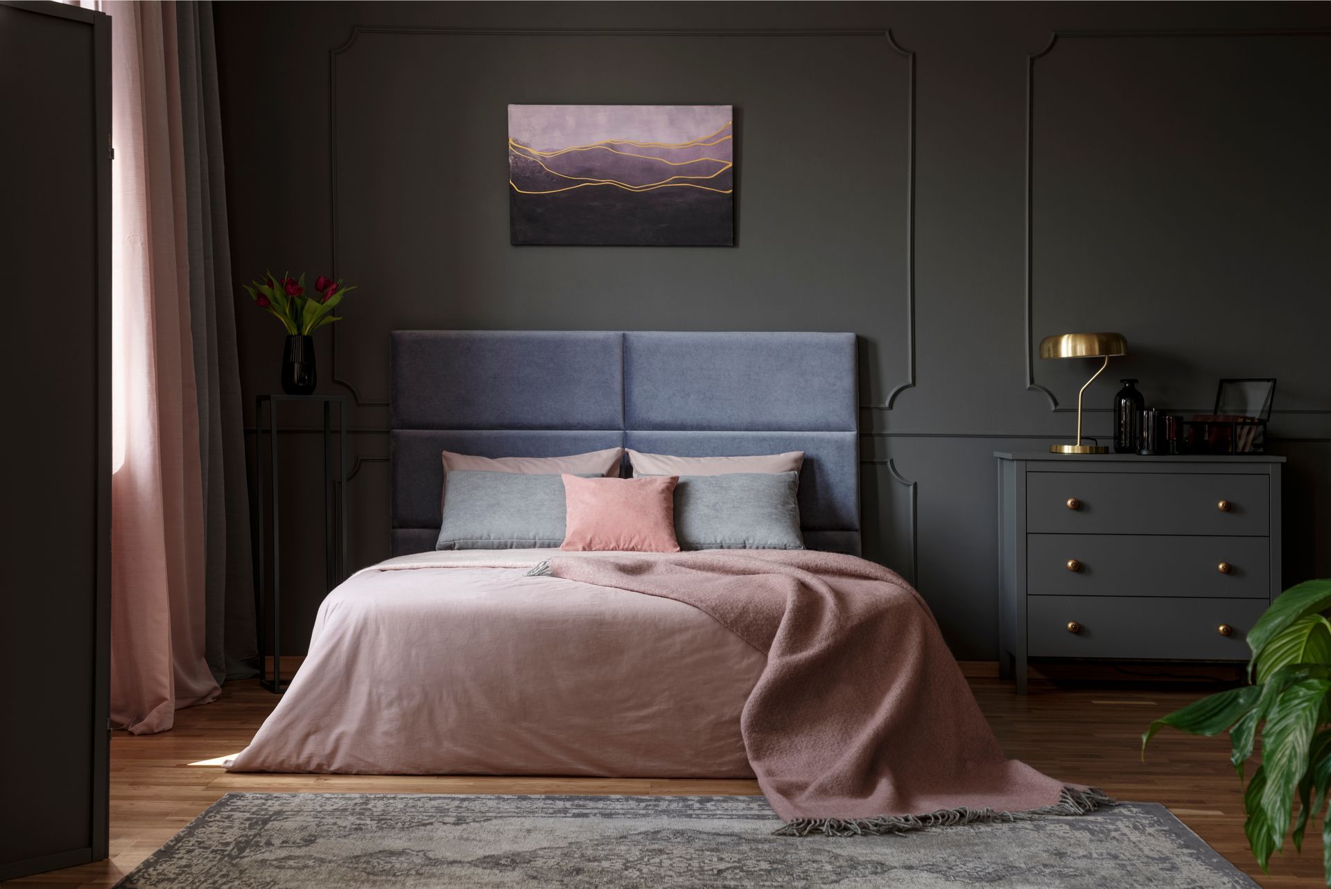 Bedroom with gray walls, blue bed, pink bedding, and dark gray dresser with gold lamp.