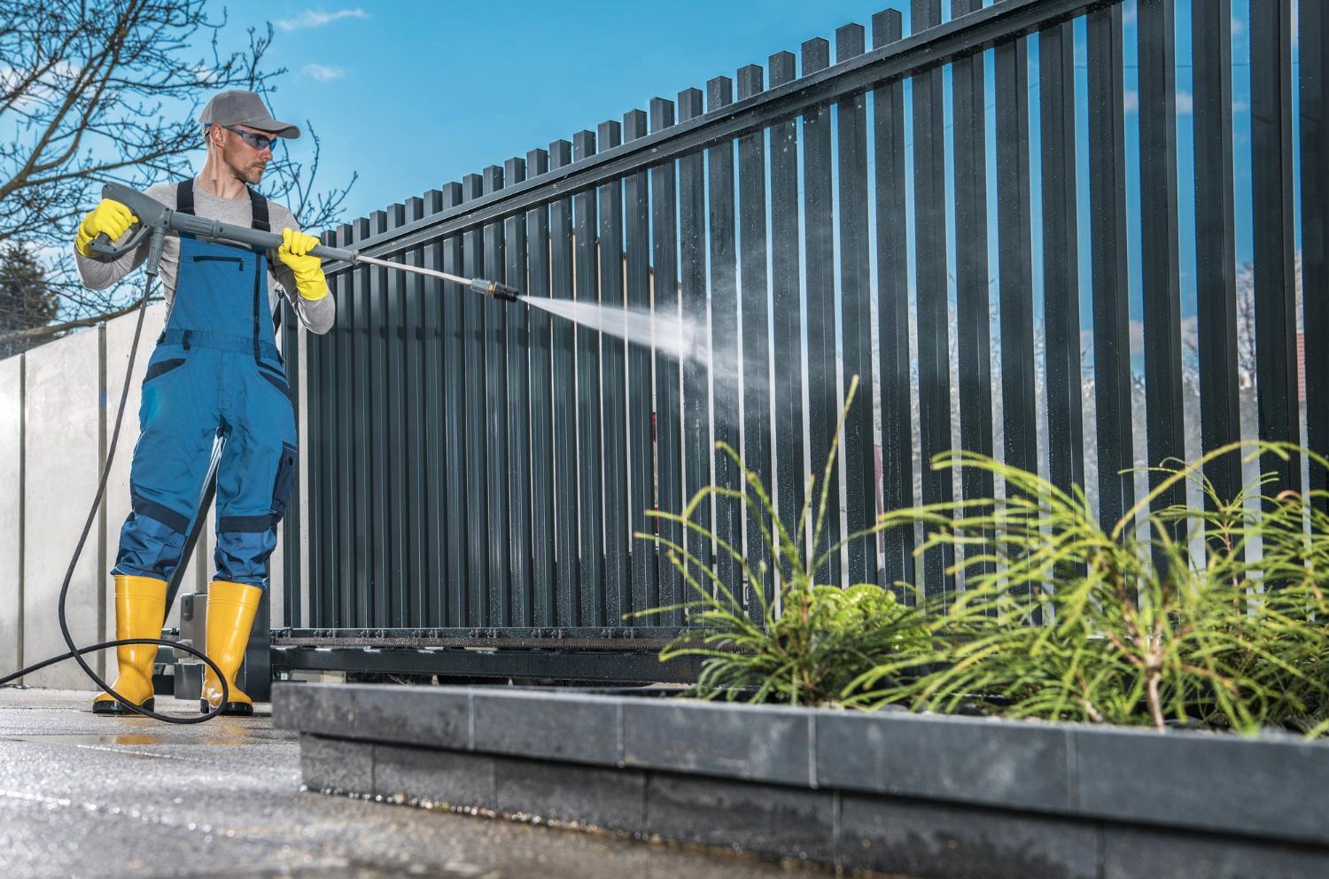 A man is cleaning a fence with a high pressure washer.