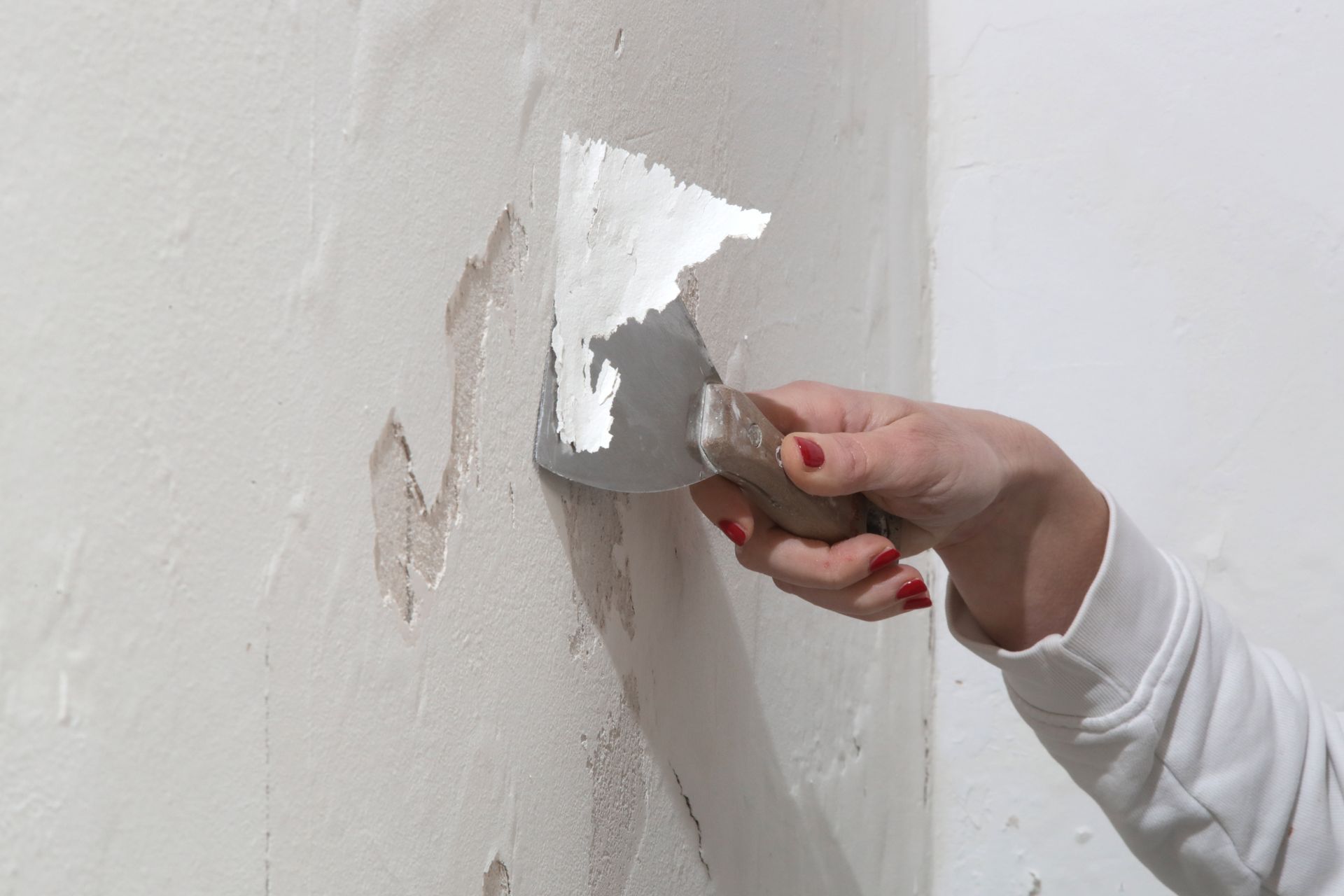 Hand using a putty knife to scrape away white wall plaster.