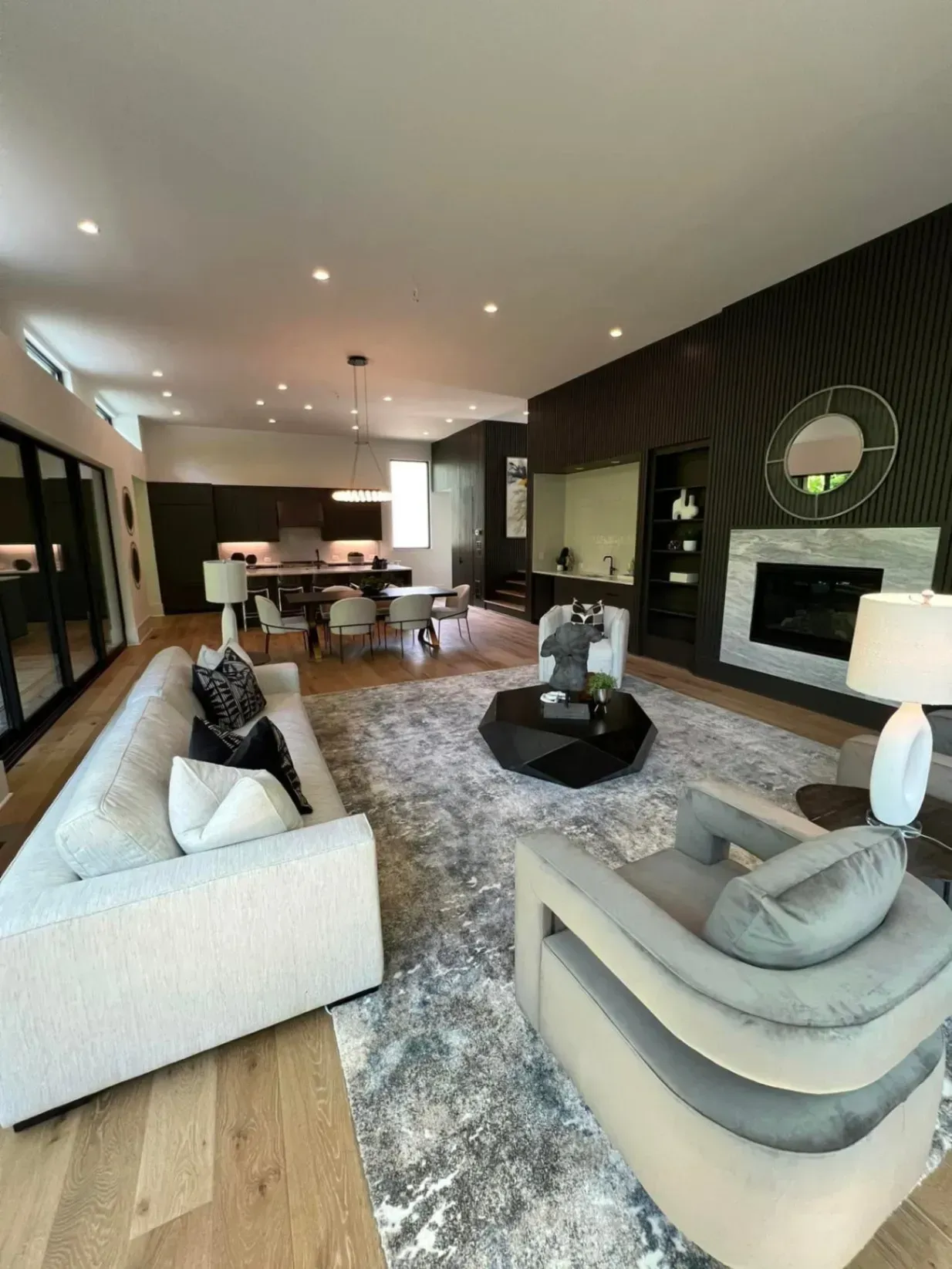 Modern living room with a couch, armchair, rug, fireplace, and kitchen visible in the background.