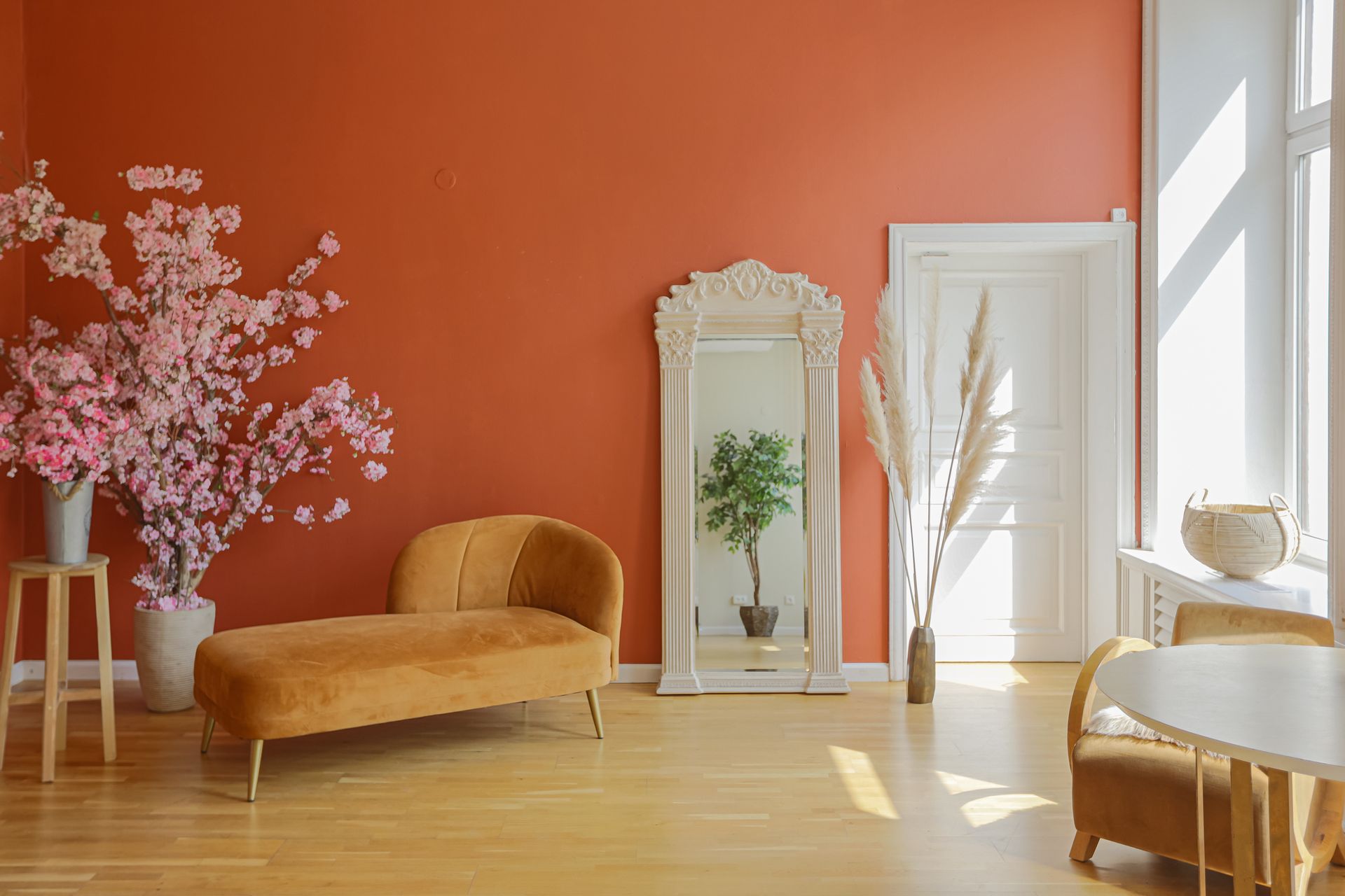 Room with terracotta walls, chaise lounge, decorative mirror, cherry blossom branches, and a white door.