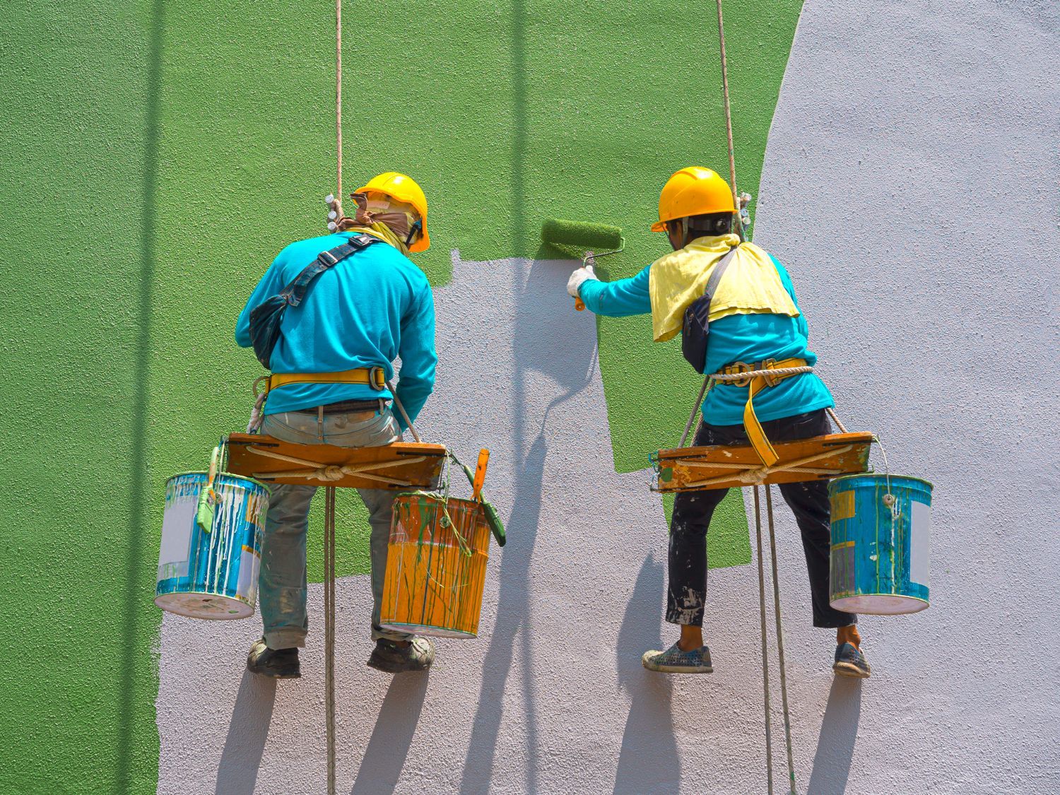 A man and a woman are painting a wall on a rope.