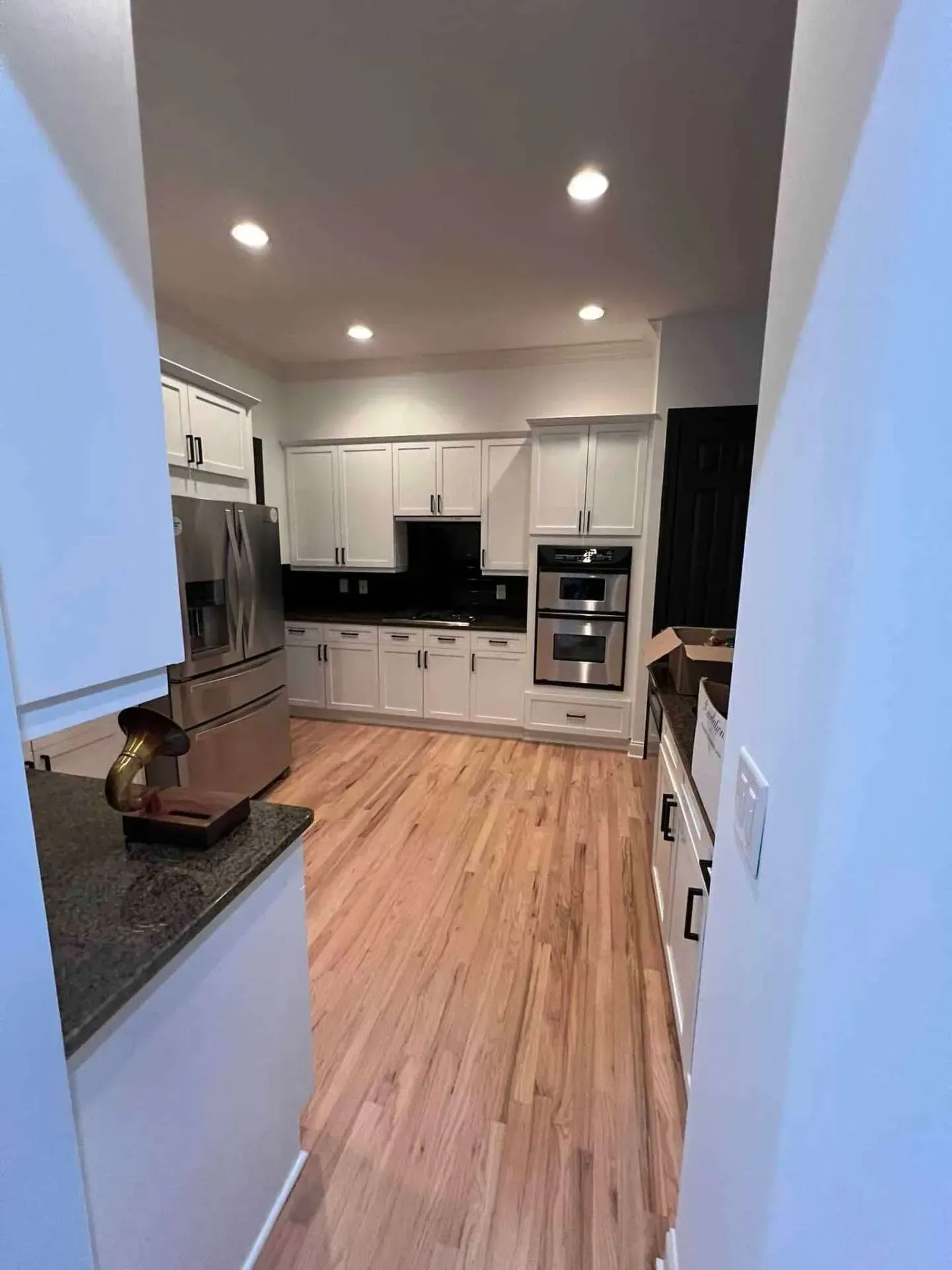 A kitchen with hardwood floors , white cabinets and stainless steel appliances.