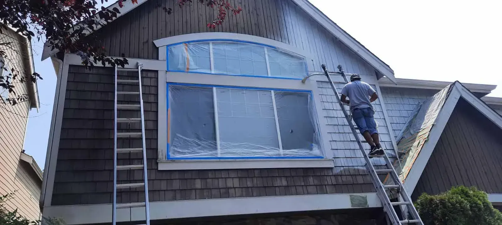 A man on a ladder is painting the side of a house.