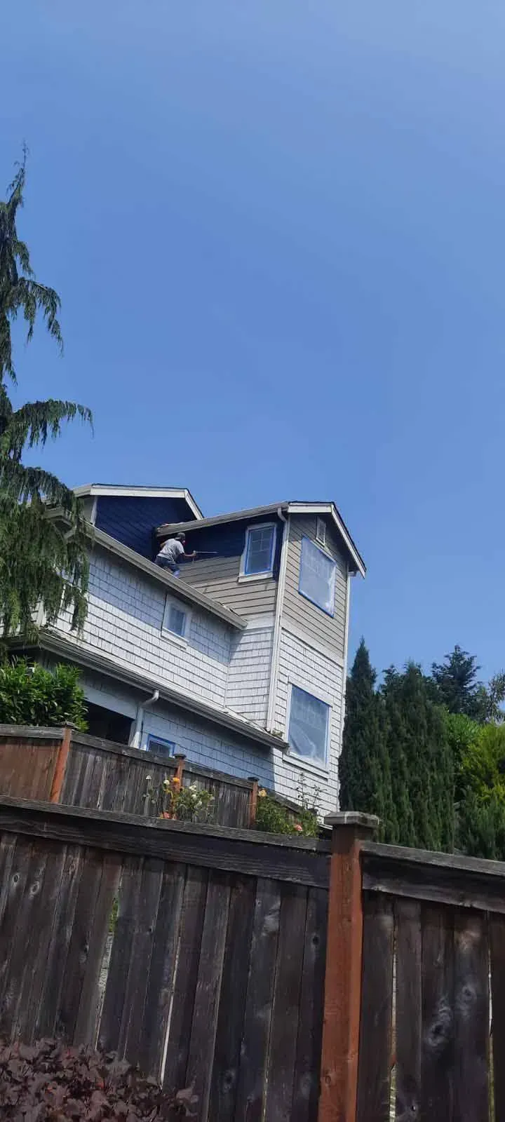 A large white house with a blue roof is behind a wooden fence.