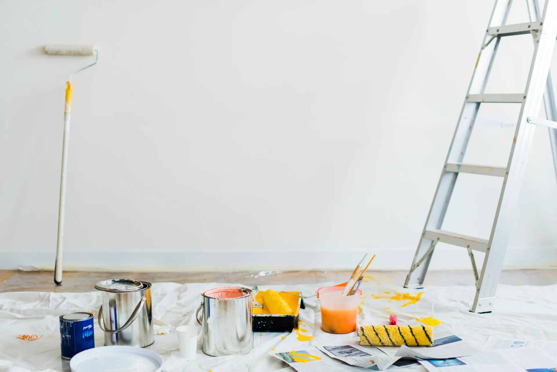 Paint supplies, roller, and ladder against a white wall.