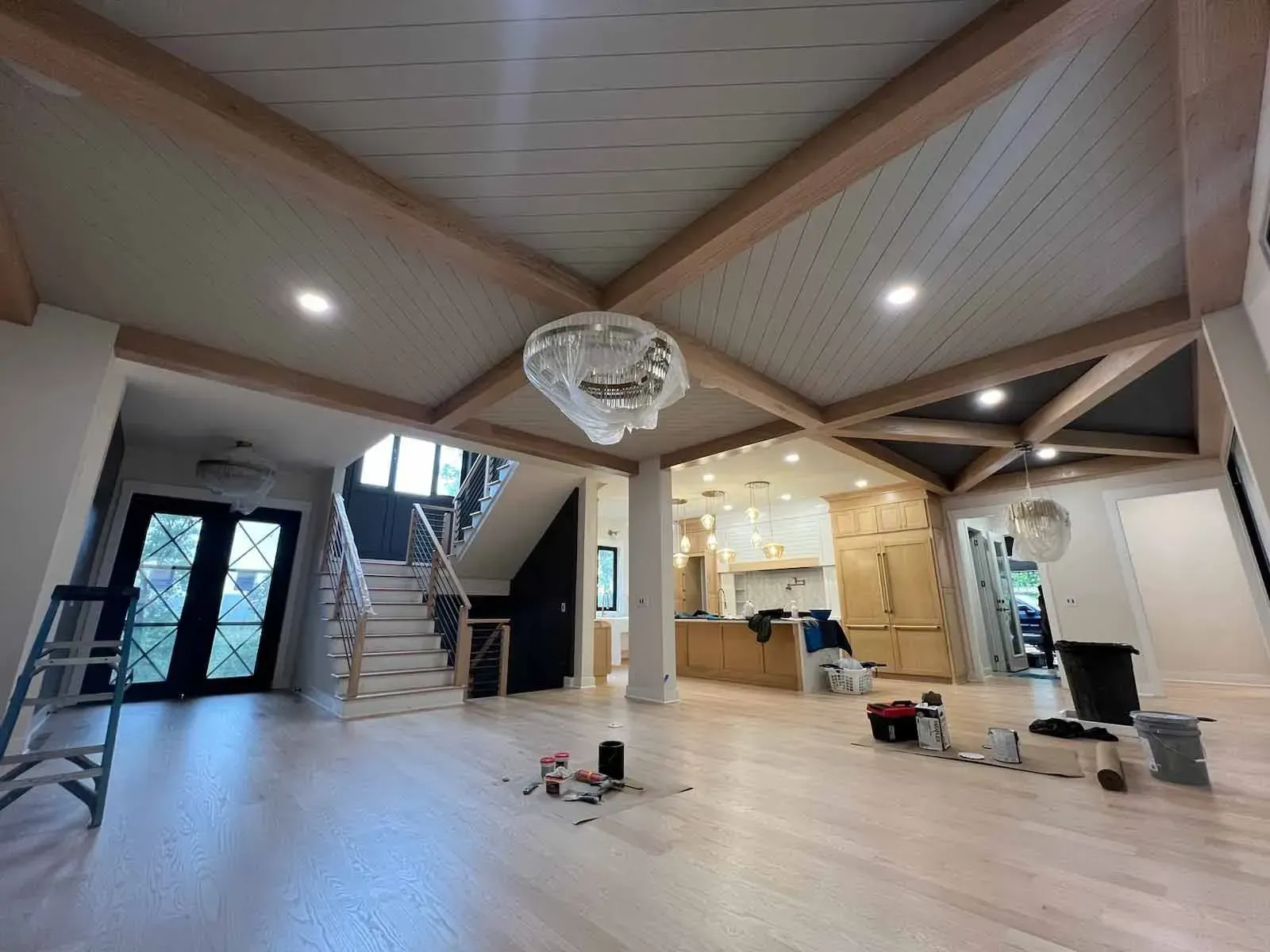 Spacious room with light wood floors, exposed beams, and a large chandelier.