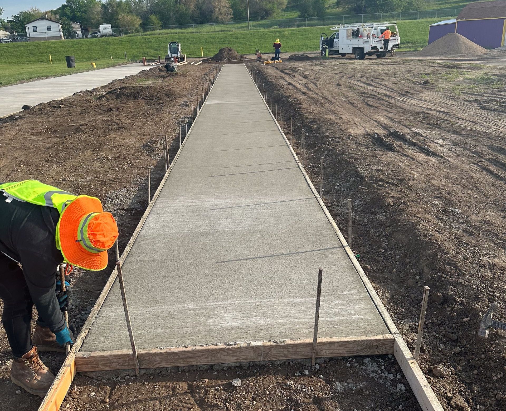 A person is using a broom to spread concrete on a sidewalk.