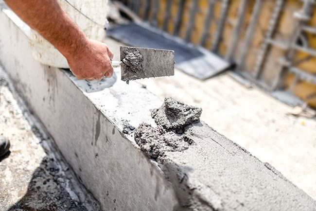 A man is using a trowel to spread cement on a concrete wall.