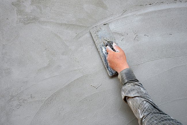 A person is plastering a wall with a trowel.