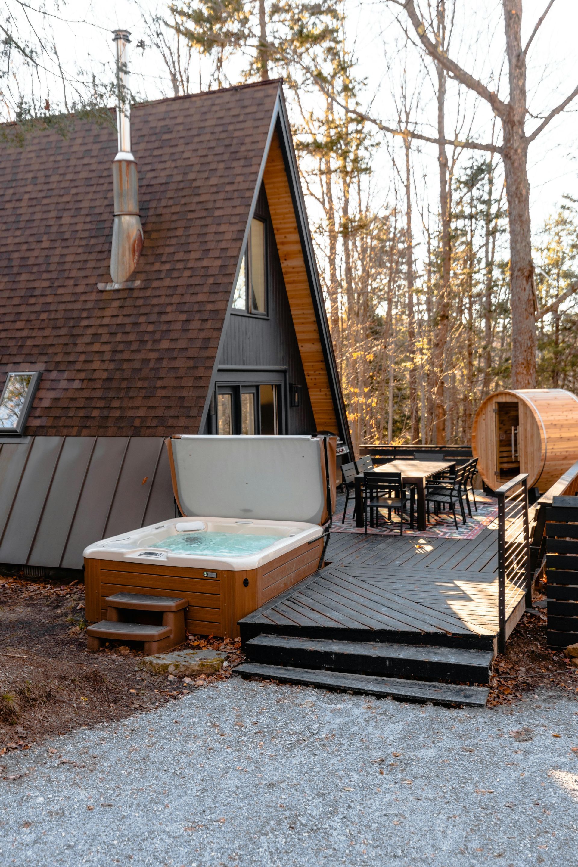 A-frame cabin with hot tub on deck, outdoor seating, and sauna in a wooded setting.