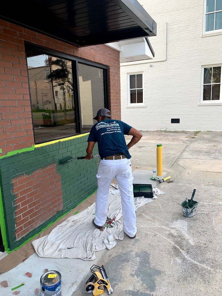 A man is painting a brick wall outside of a building.