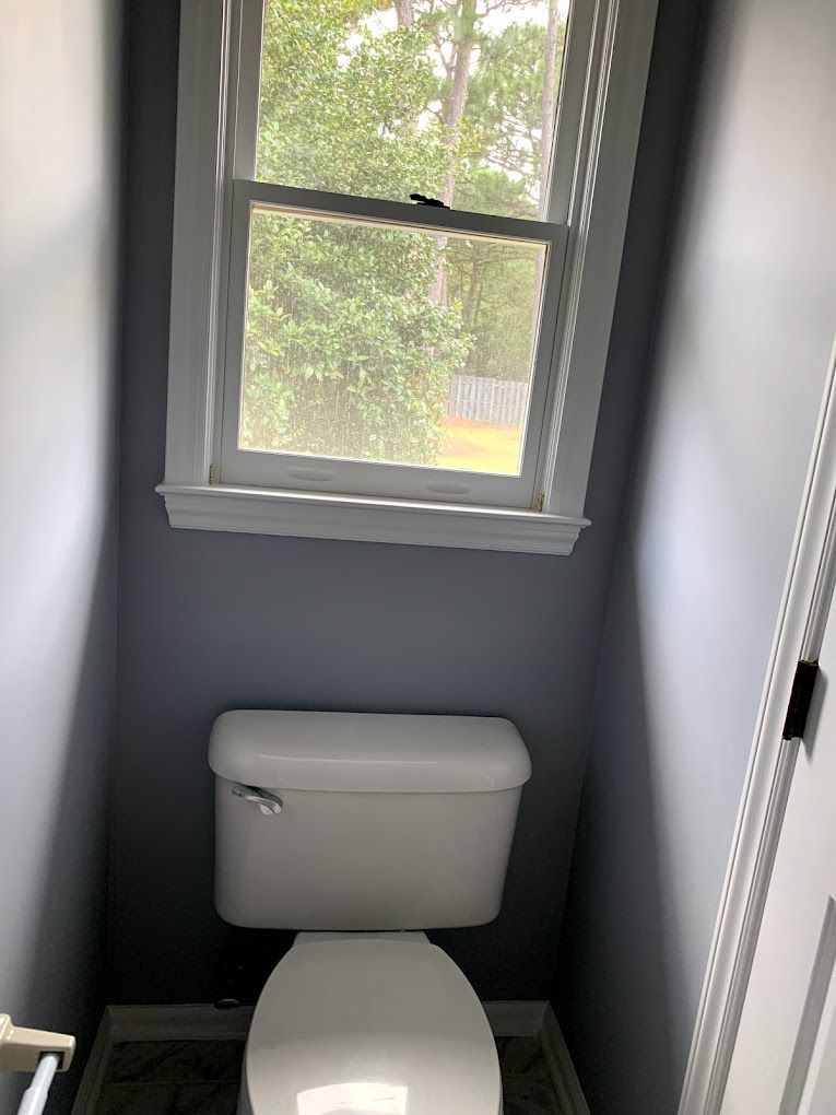 A toilet is sitting in a small bathroom next to a window.
