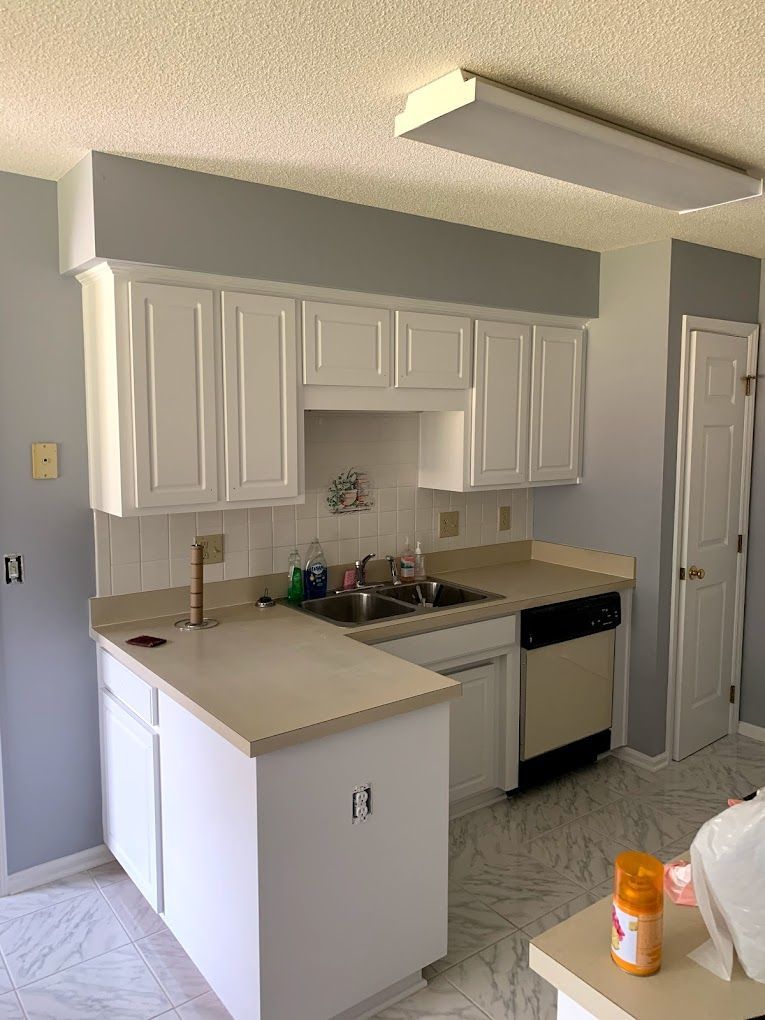 A kitchen with white cabinets , a sink , and a dishwasher.