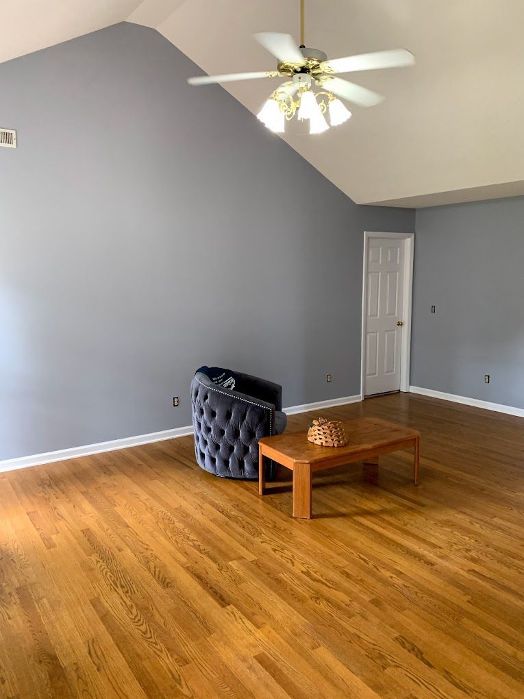 A living room with hardwood floors , a chair , a coffee table and a ceiling fan.