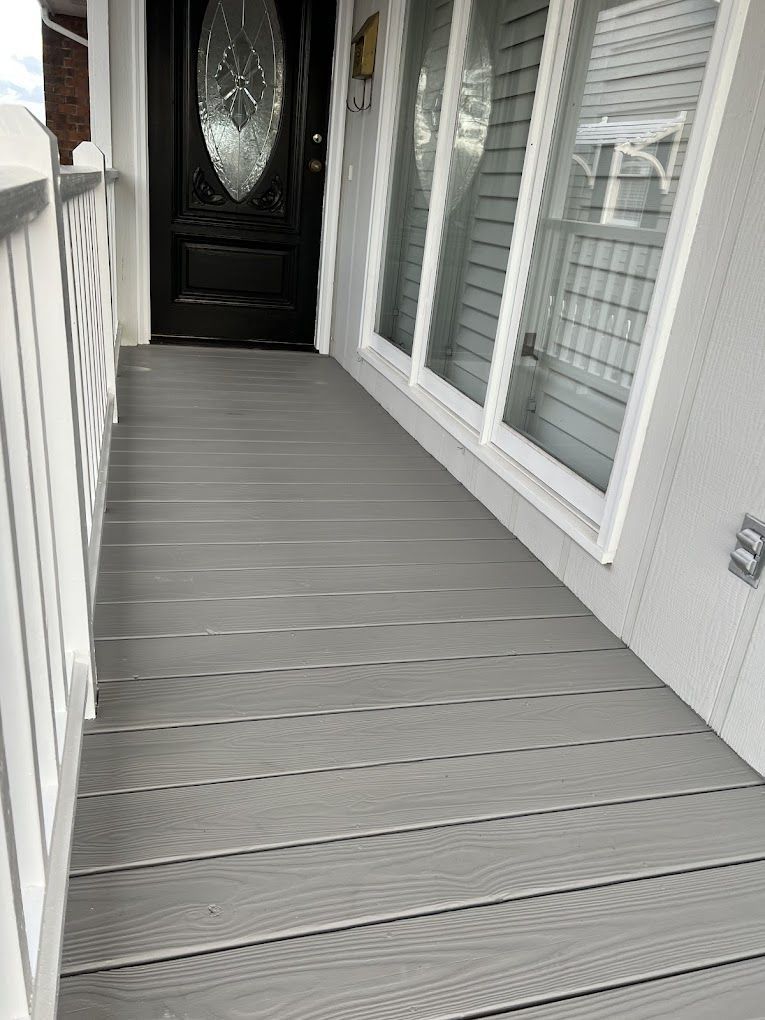 A gray porch with a black door and white railing.