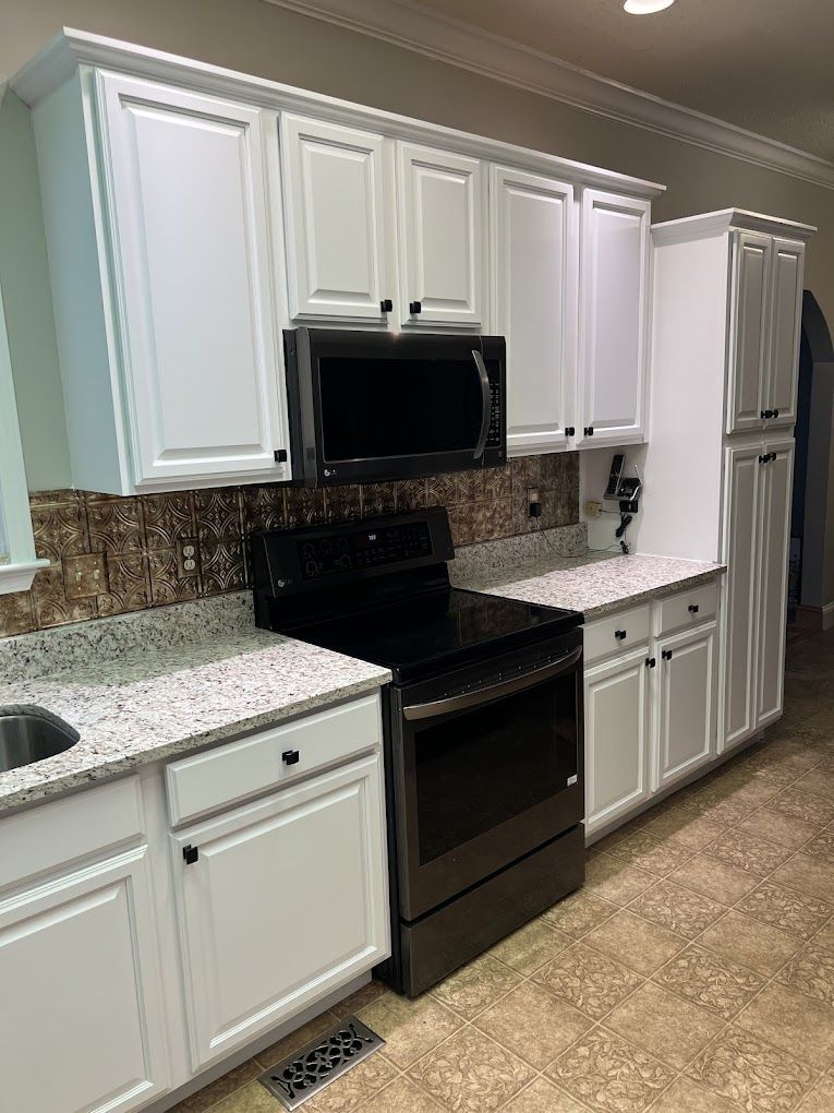 A kitchen with white cabinets , a black stove , a microwave , and a sink.