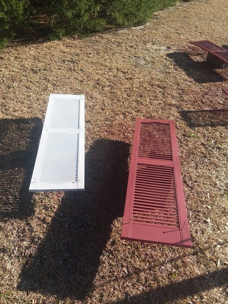 A white shutter and a red shutter are sitting on the ground.