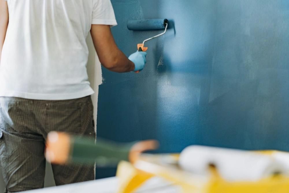 A man is painting a blue wall with a paint roller.