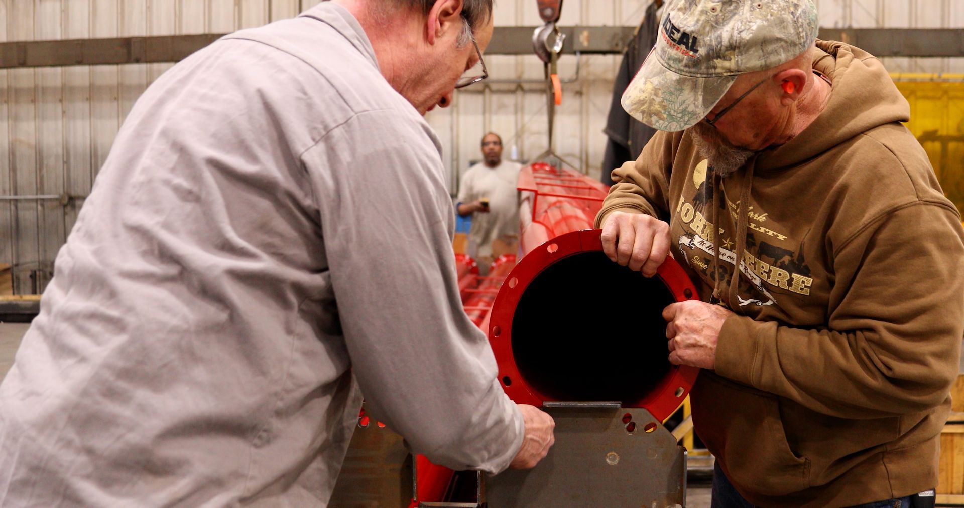 Two men are working on a red pipe in a factory.