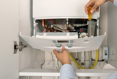 Technician adjusting an open white boiler with a screwdriver inside a utility cabinet