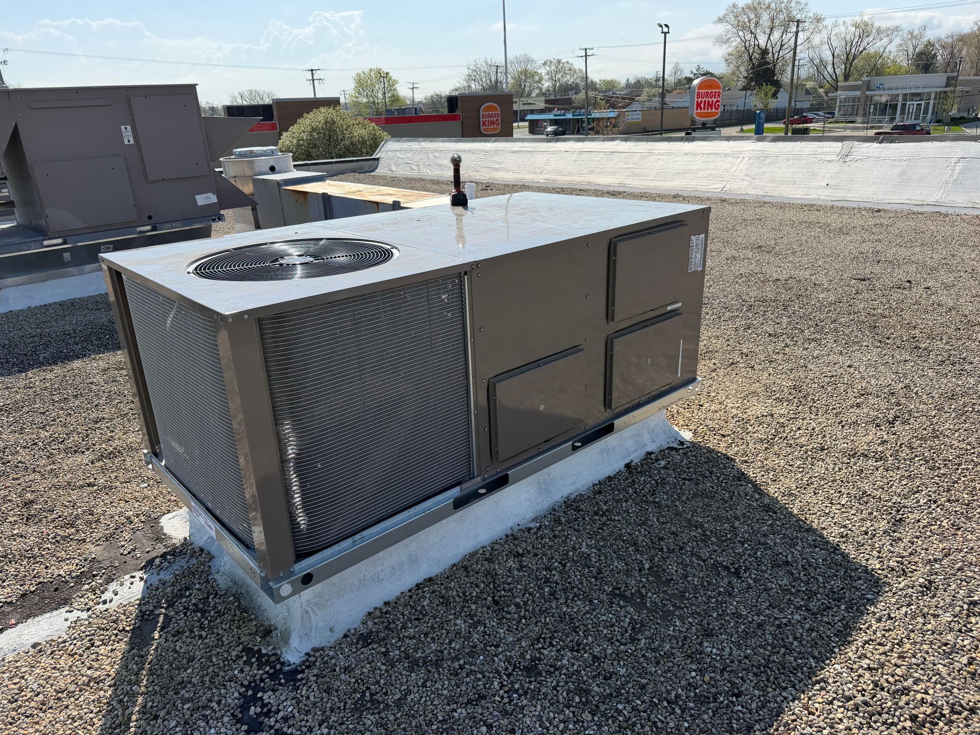 Gray rooftop HVAC unit on gravel with circular fan grilles and vent panels