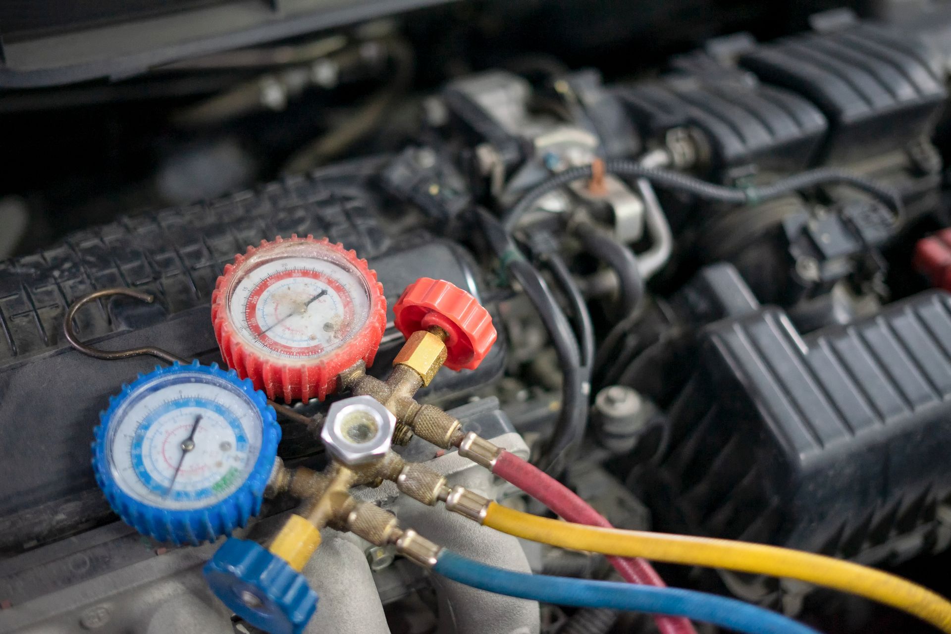 Car engine with gauges and hoses connected for AC diagnostics.