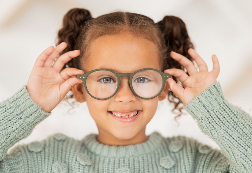 Una niña que lleva gafas y un suéter verde está sonriendo.