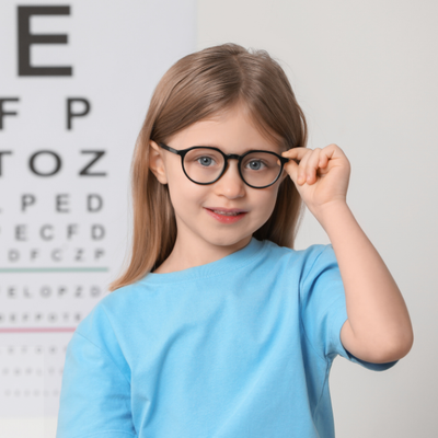Una niña con gafas está parada frente a una tabla optométrica.
