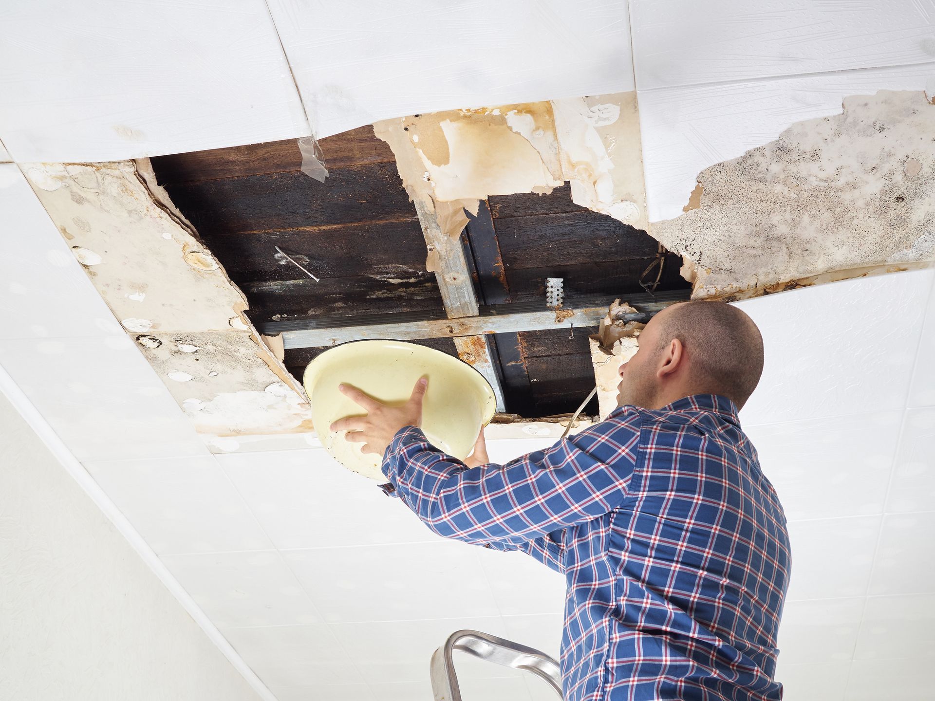 A man is looking through a hole in the ceiling while holding a plate.